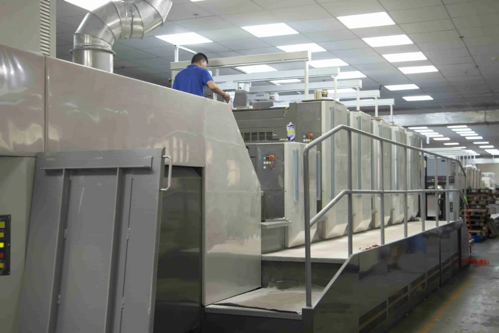 Worker inspecting large printing press machine in factory